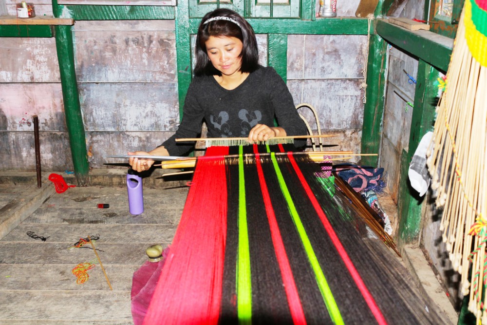 A young woman weaves traditional apparel by method of the traditional process of weaving.
